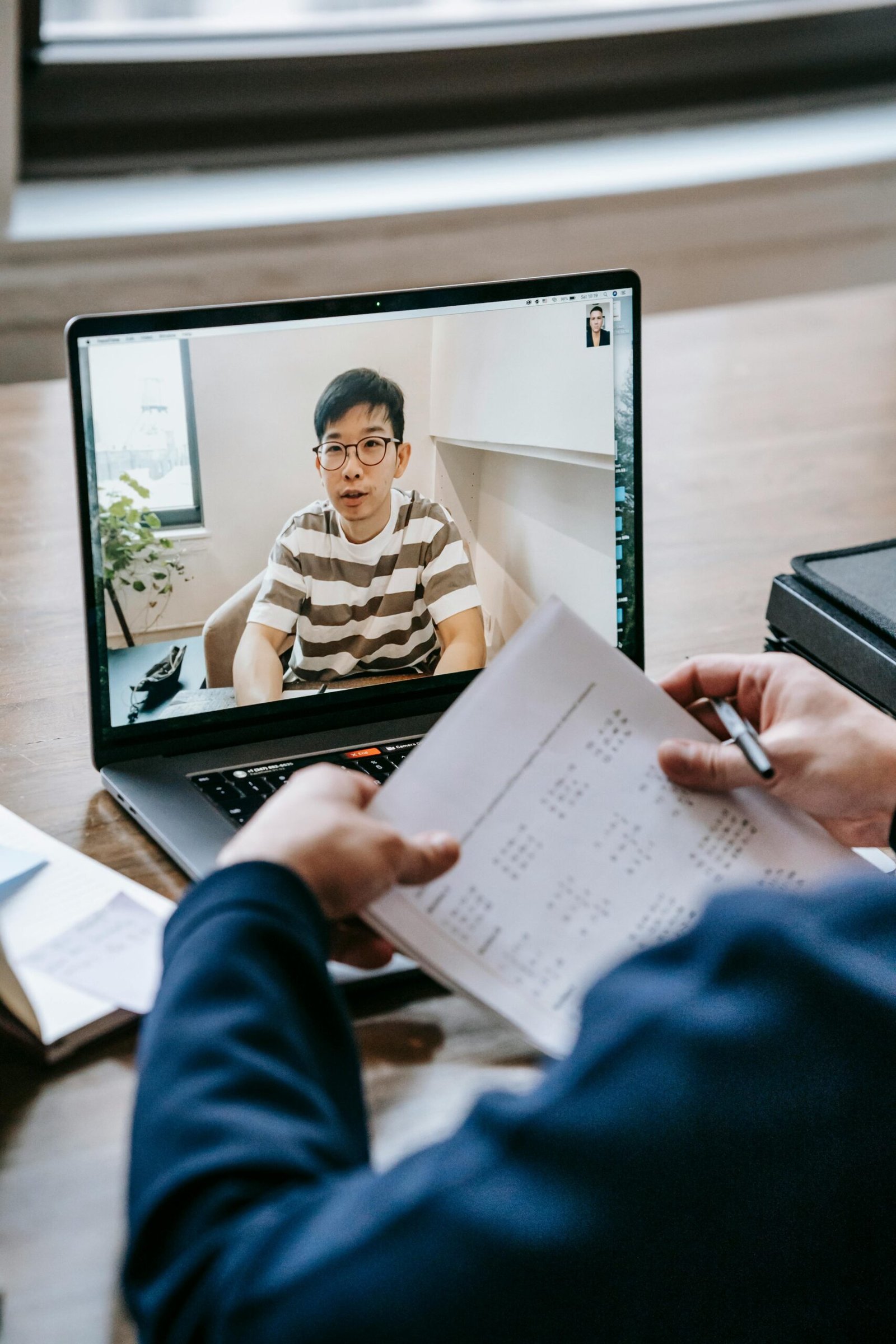 Adult participating in a video conference with paperwork on a desk.